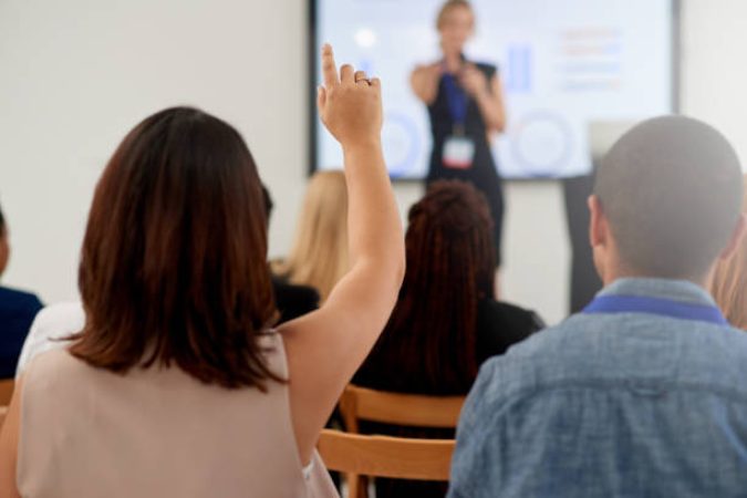 Rearview shot of an audience member raising their hand to ask a question during a business conference