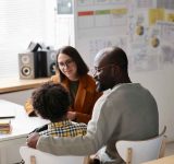 Rear view of African American father talking to teacher about school success of his son